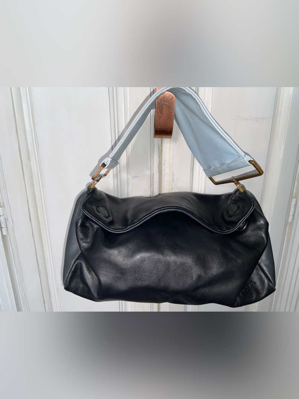 black leather Prada shoulder bag with light blue straps and embossed logo detail